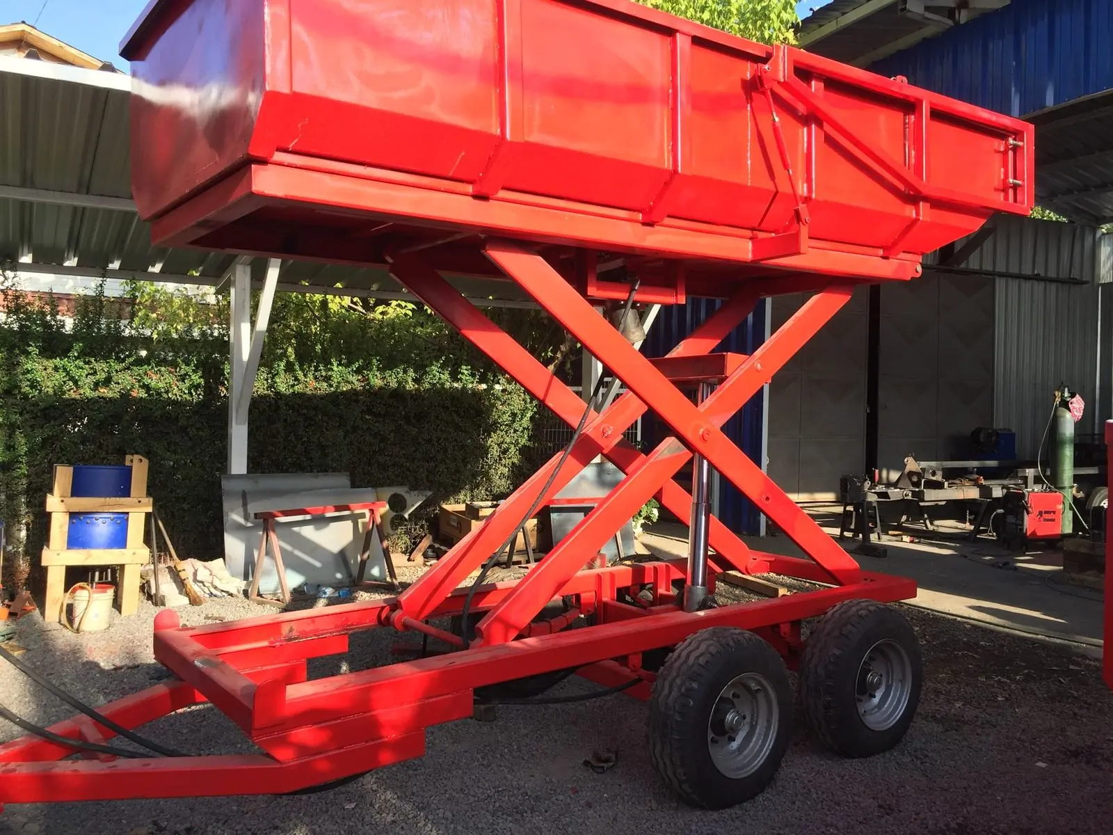 Carro tolva rojo con la tolva elevada por tijera, bajo el techo del taller.