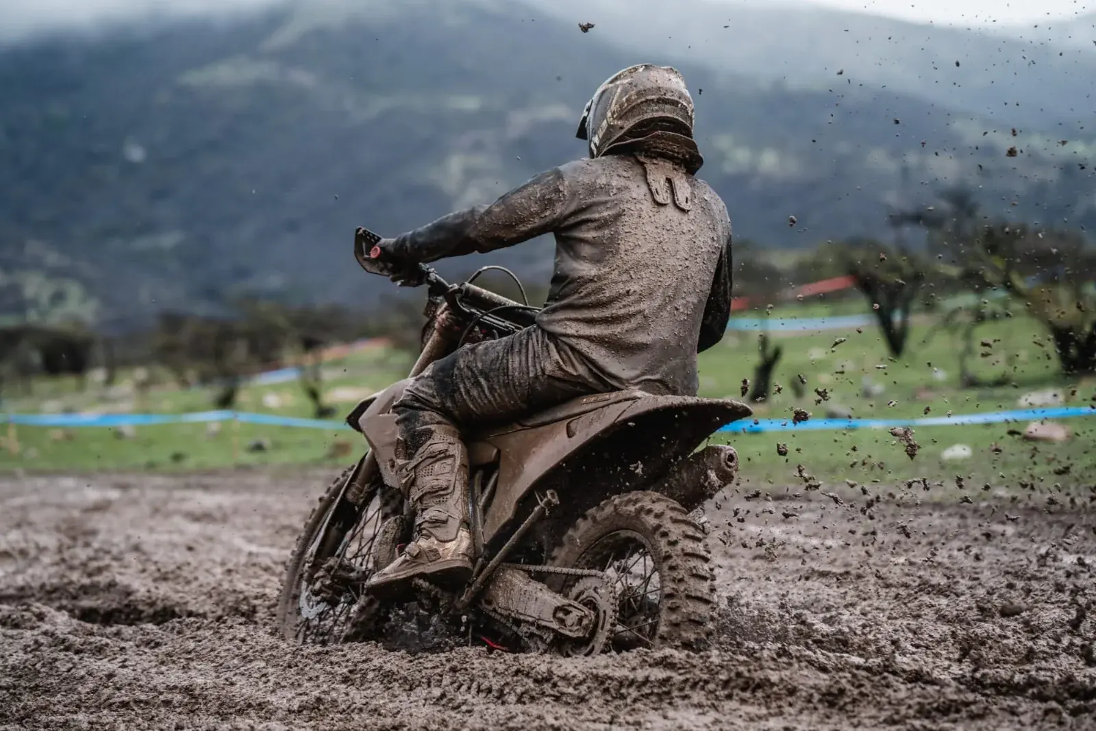 Moto de enduro cruzando un tramo embarrado, con el cerro al fondo.