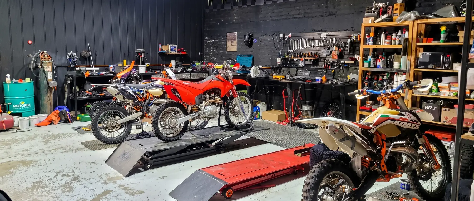 Taller con tres motos sobre elevadores y herramientas en la pared.
